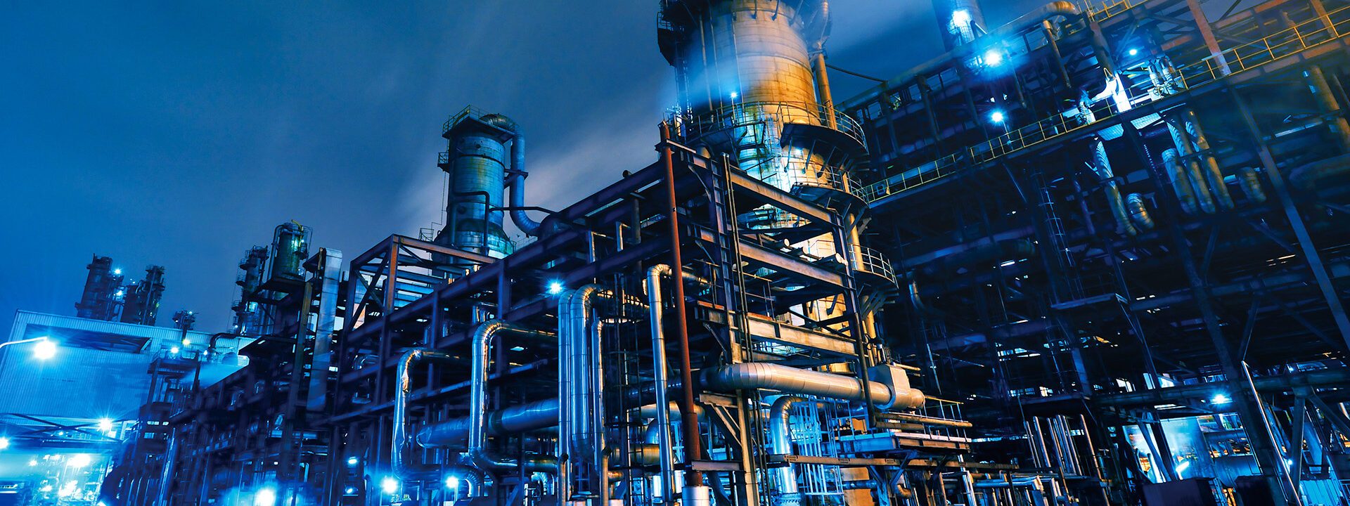 Chemical processing plant pipework lit blue at night